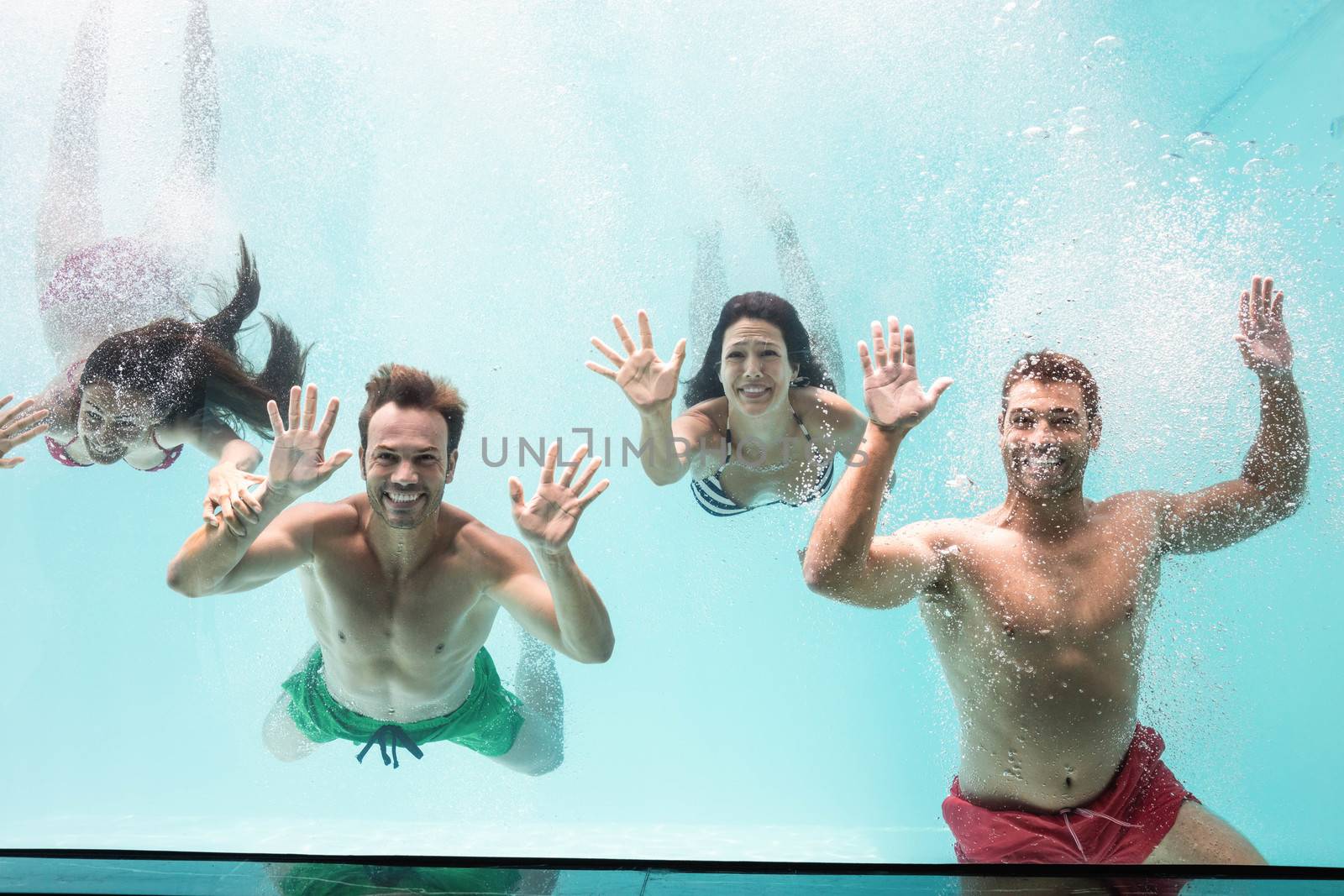 Two couples enjoying and swimming underwater in swimming pool