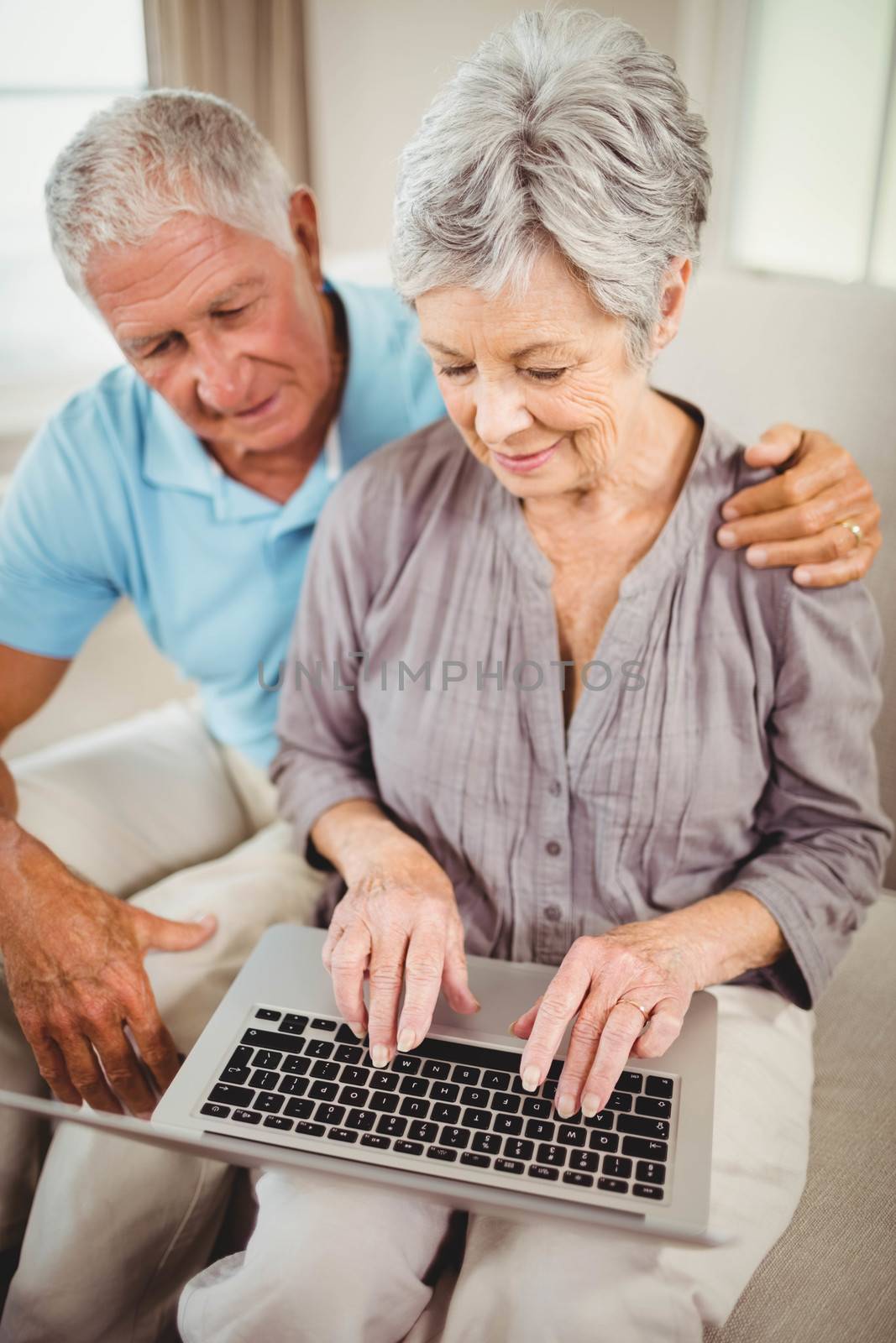 Senior woman sitting with man on sofa and using laptop in living room