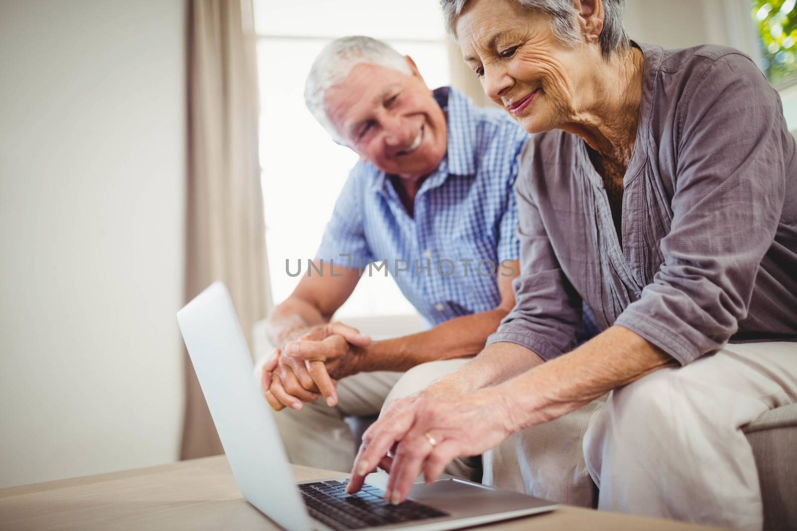 Senior woman sitting with man on sofa and using laptop in living room