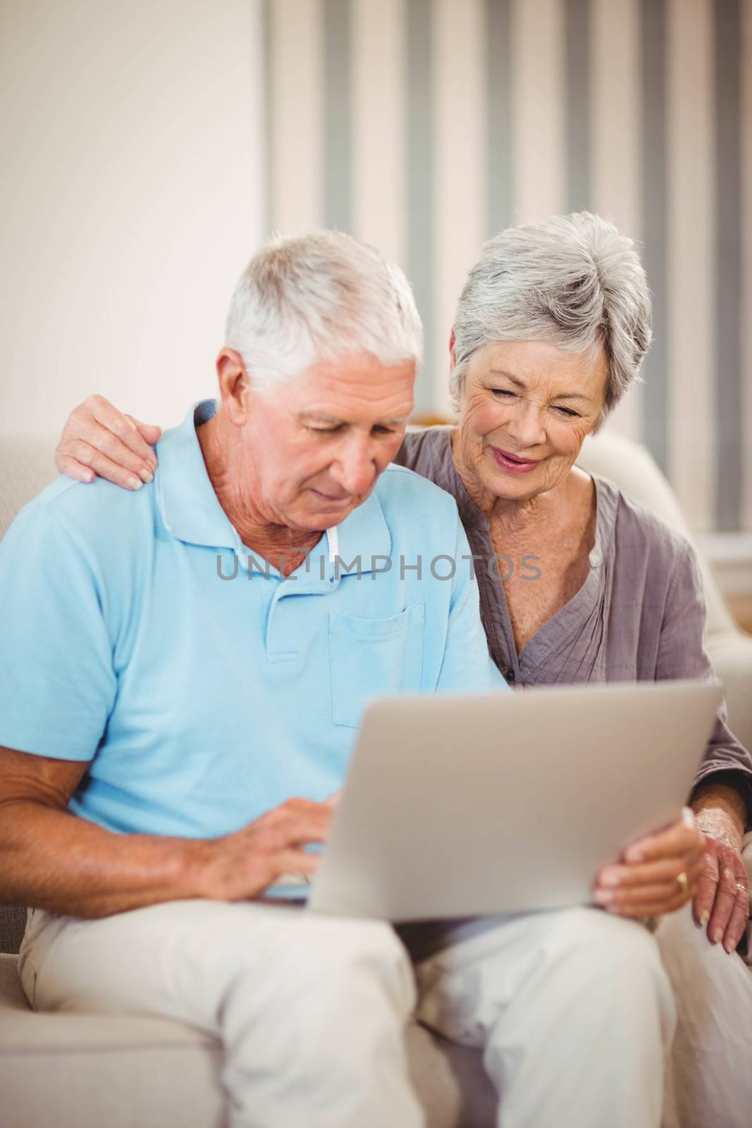Senior man sitting with woman on sofa and using laptop in living room
