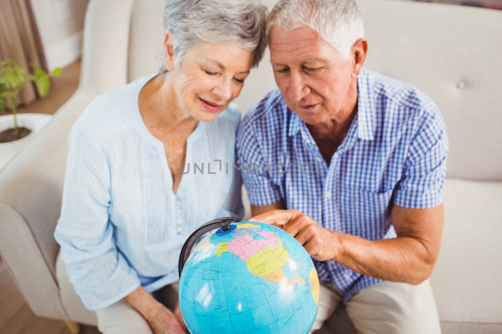 Senior couple sitting on sofa and looking at a globe in living room