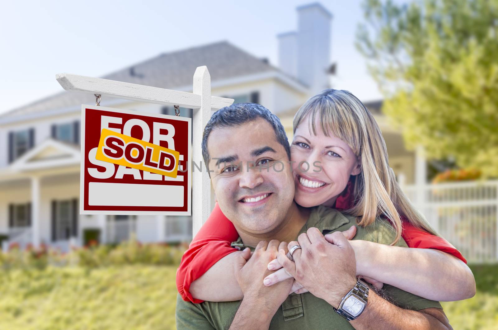 Happy Mixed Race Couple in Front of Sold Home For Sale Real Estate Sign and House.