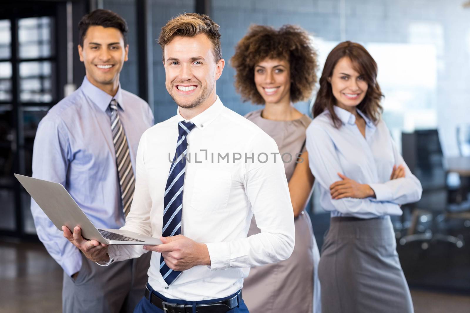 Businessman standing with a laptop while his team standing in behind him in office