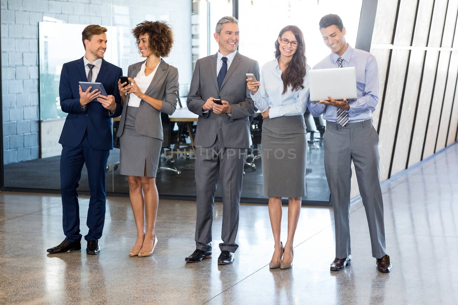 Businesspeople standing in a row and using mobile phone, lap top and digital tablet in office