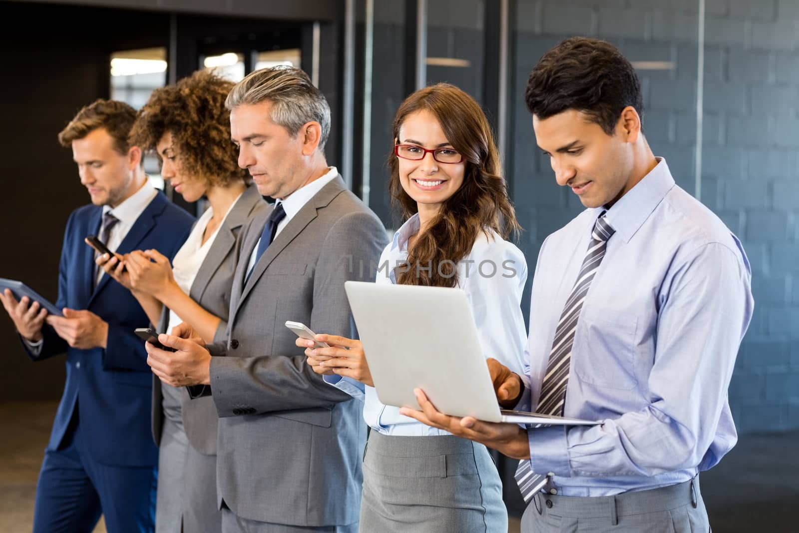 Businesspeople standing in a row and using mobile phone, lap top and digital tablet in office