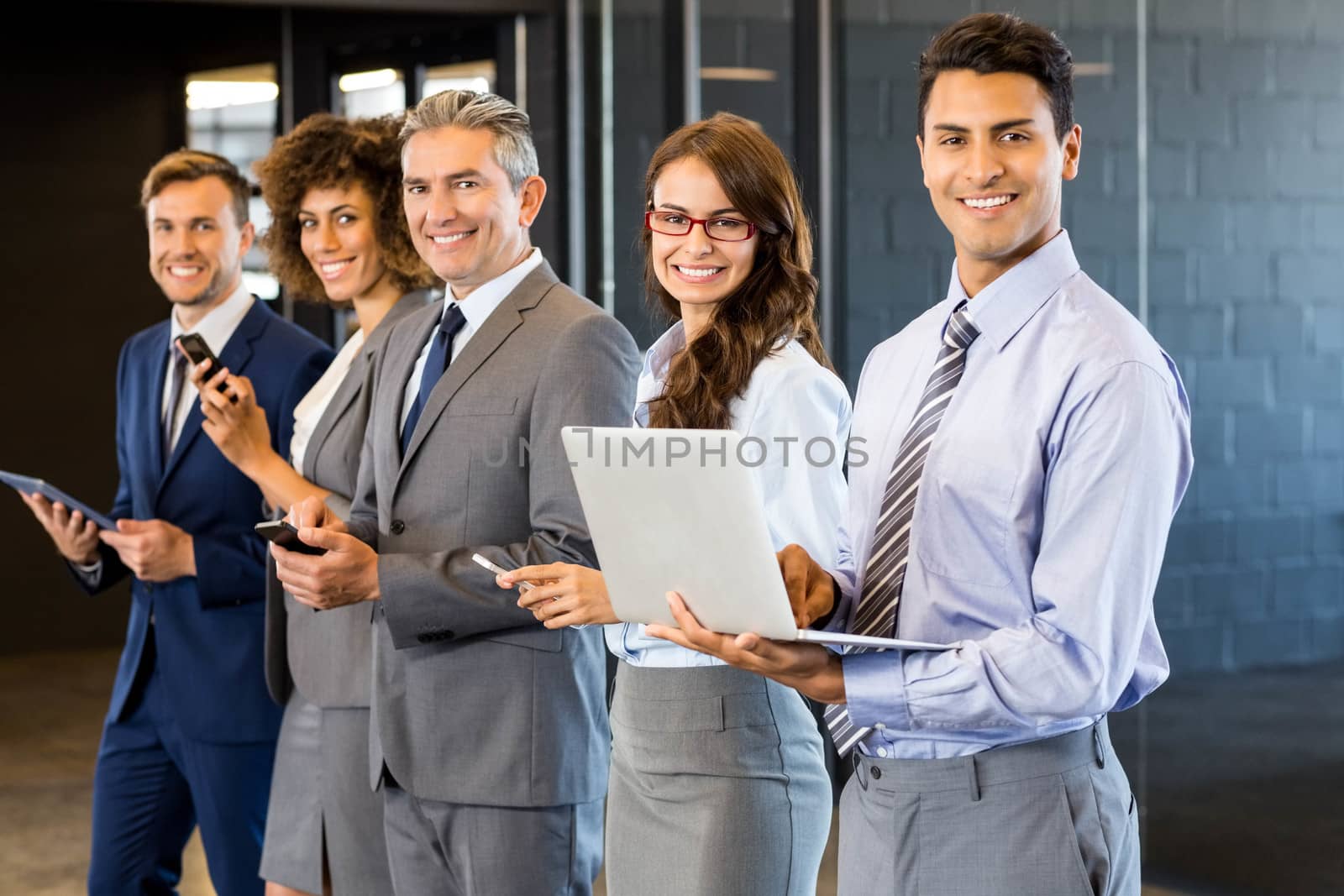Businesspeople standing in a row and using mobile phone, lap top and digital tablet in office