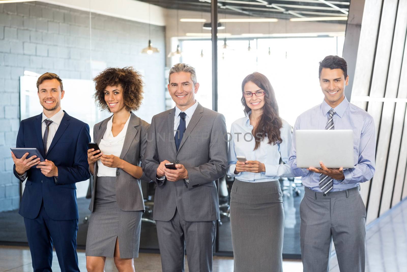 Businesspeople standing in a row and using mobile phone, lap top and digital tablet in offic