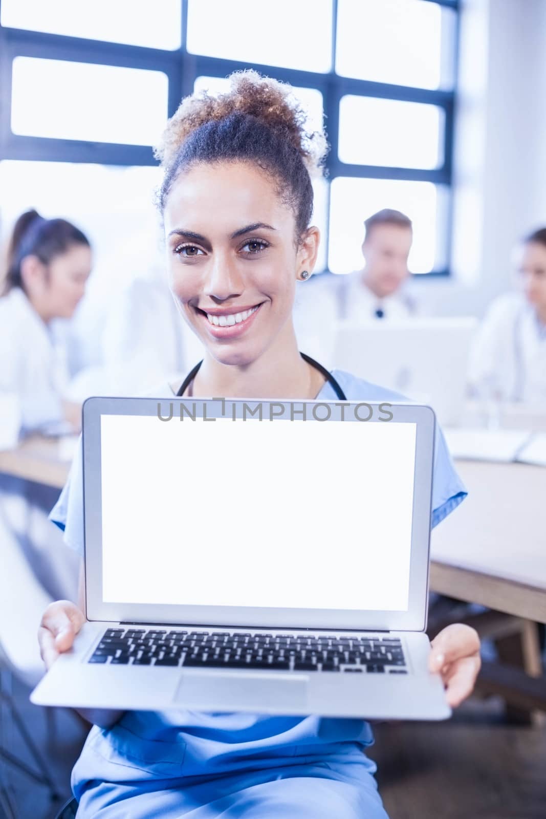 Portrait of female doctor showing laptop and other doctors discussing behind in conference room