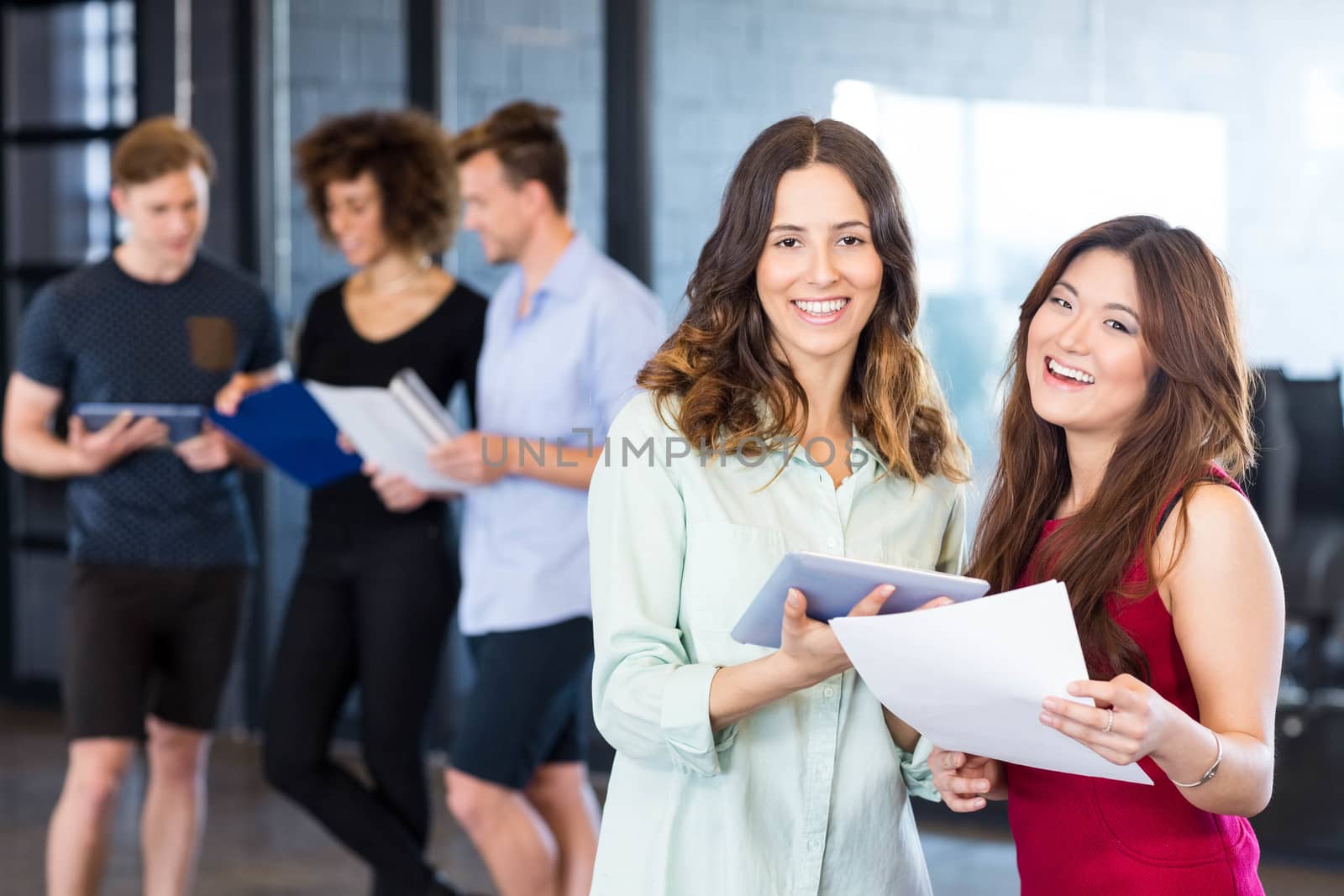 Portrait of women holding digital tablet and smiling while colleagues standing behind in office