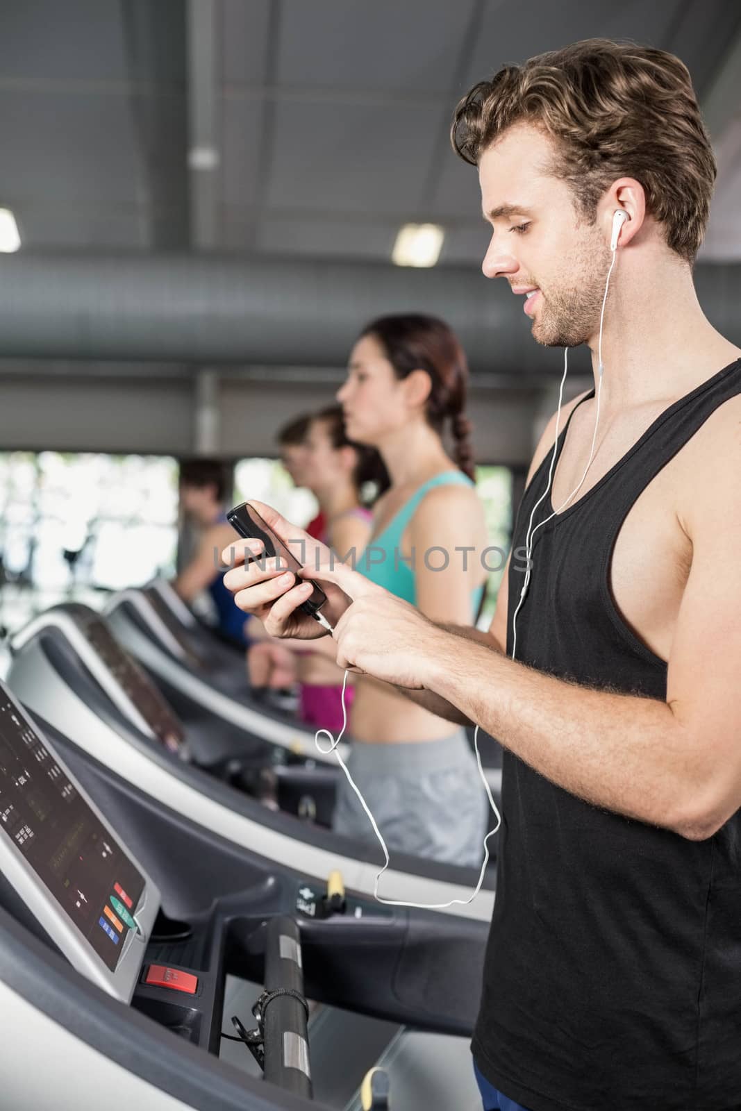 Smiling muscular man on treadmill listening to music at gym 