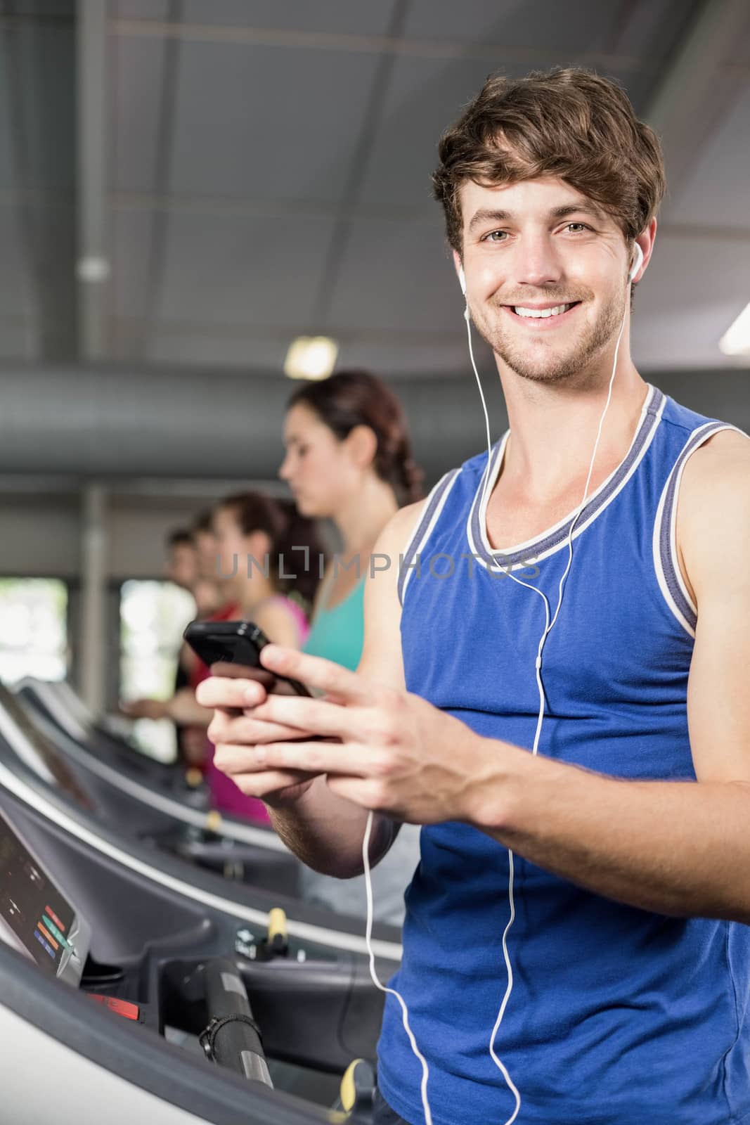 Smiling muscular man on treadmill listening to music at gym 