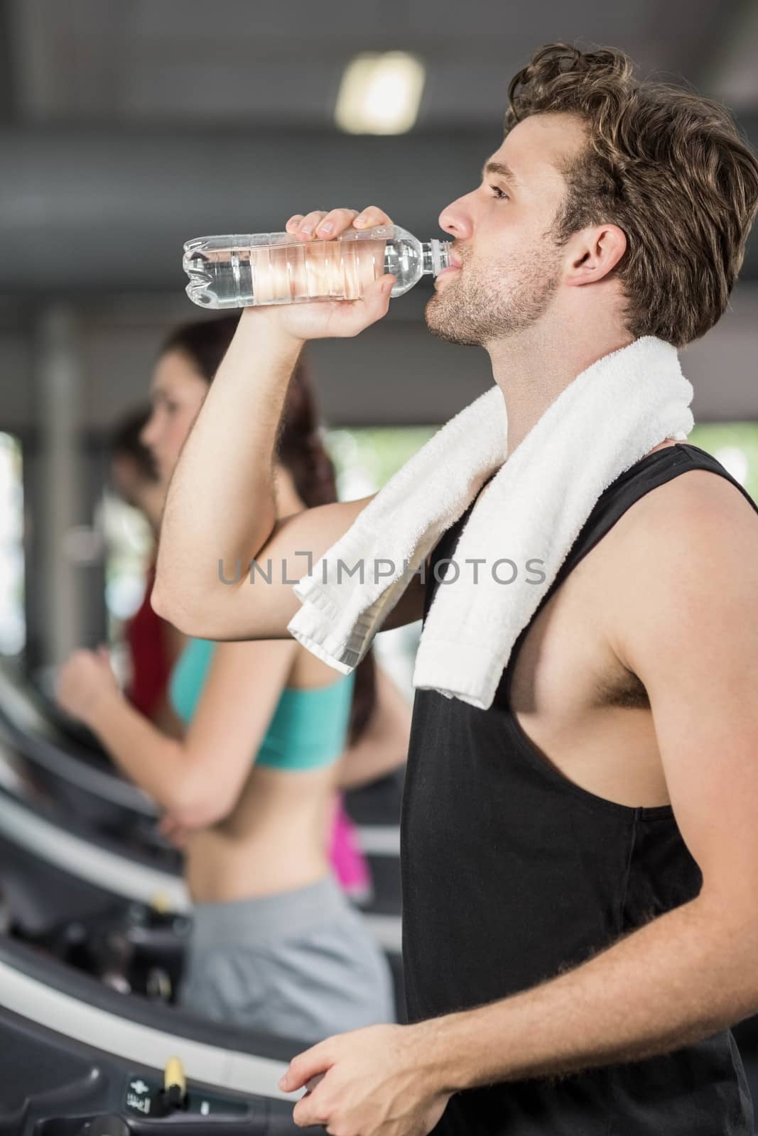 Athletic man drinking water while running on treadmill in crossfit