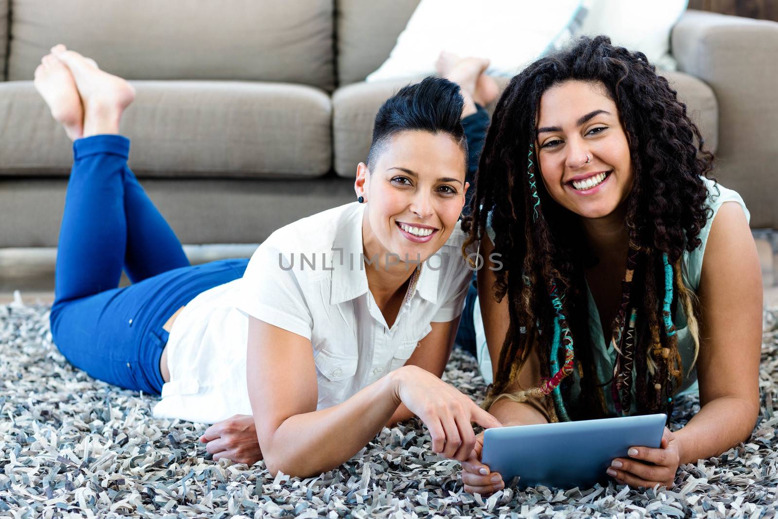 Smiling lesbian couple lying on rug and using digital tablet in living room