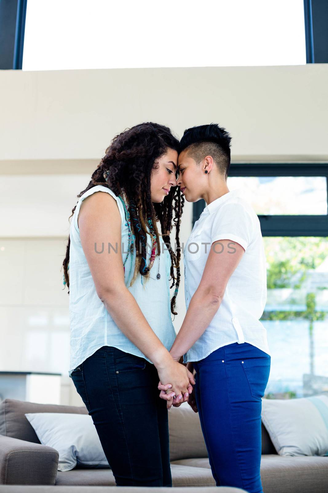Romantic lesbian couple standing face to face and holding hands in living room