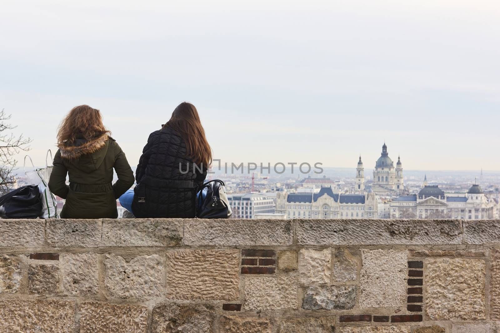 BUDAPEST, HUNGARY - FEBRUARY 02: Two girls sitting on wall enjoying the view from Buda Castle, with Gresham Palace and Saint Stephen's Basilica in the background. February 02, 2016 in Budapest.