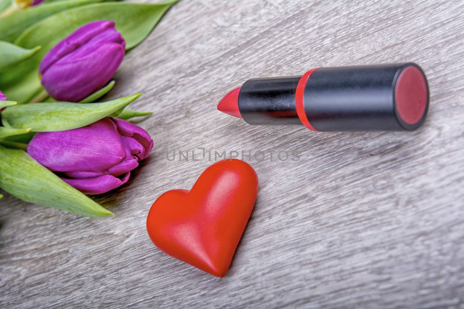 Lipstick, red heart and purple tulips on a wooden background