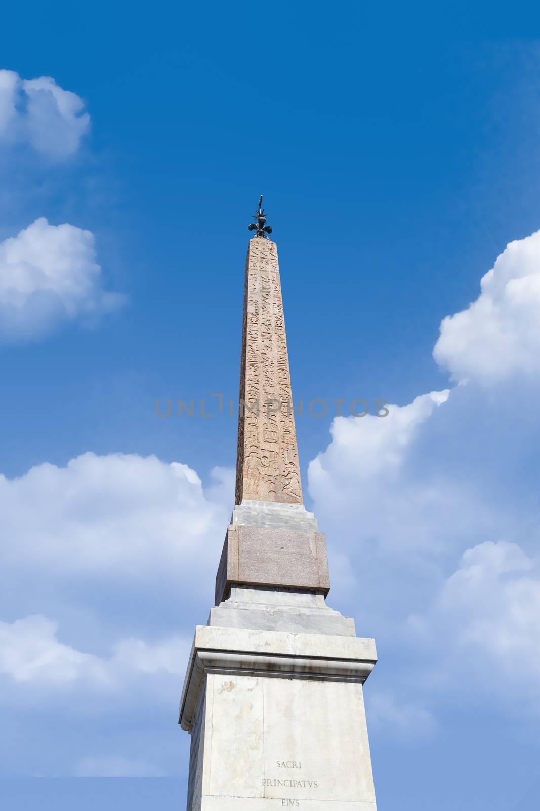 Bottom view of a column monument with hieroglyphics, on cloudy blue sky background.