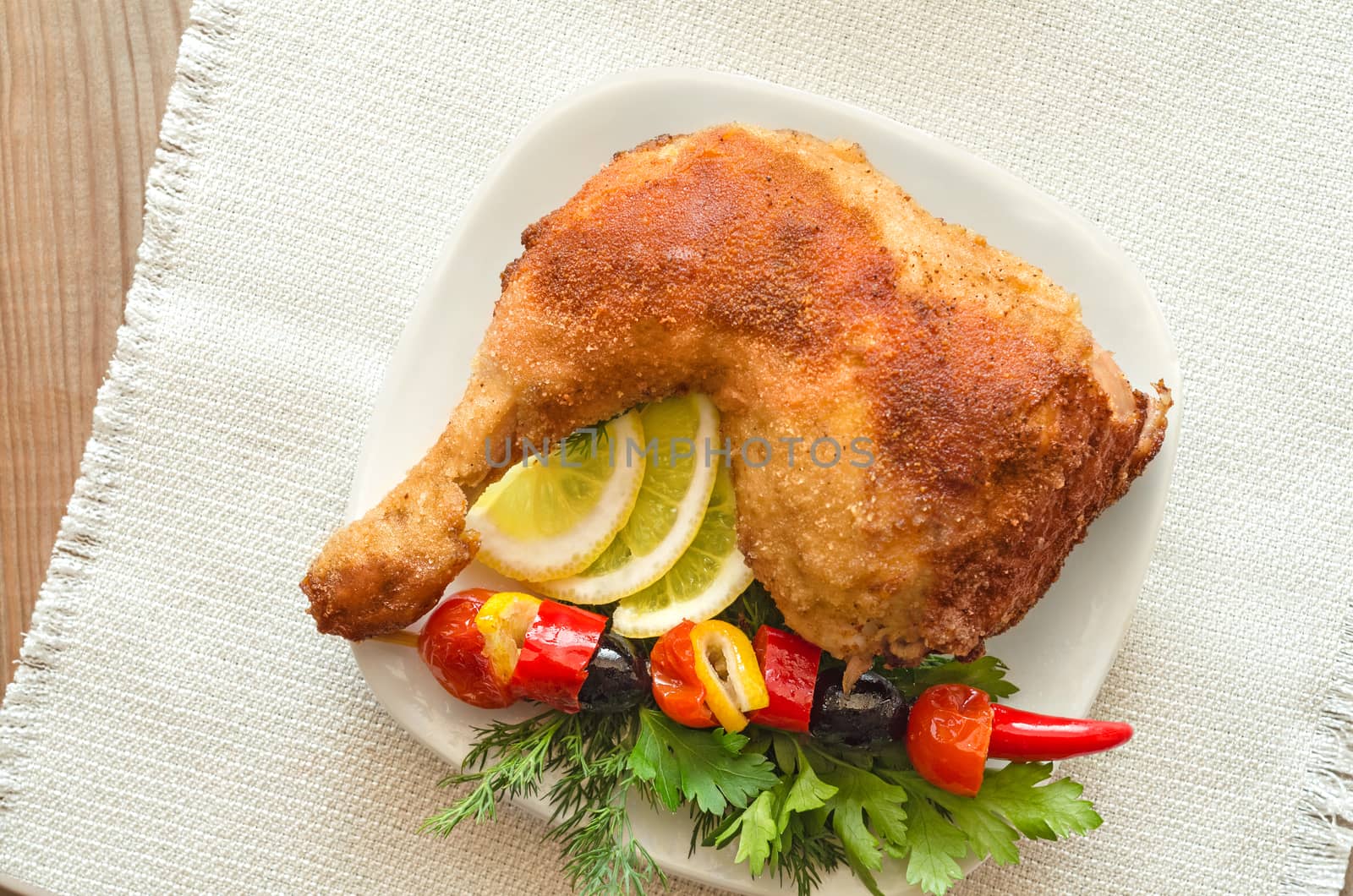 Chicken thigh in the breadcrumbs, and skewers of sweet peppers and olives. On a wooden table and a white cloth.