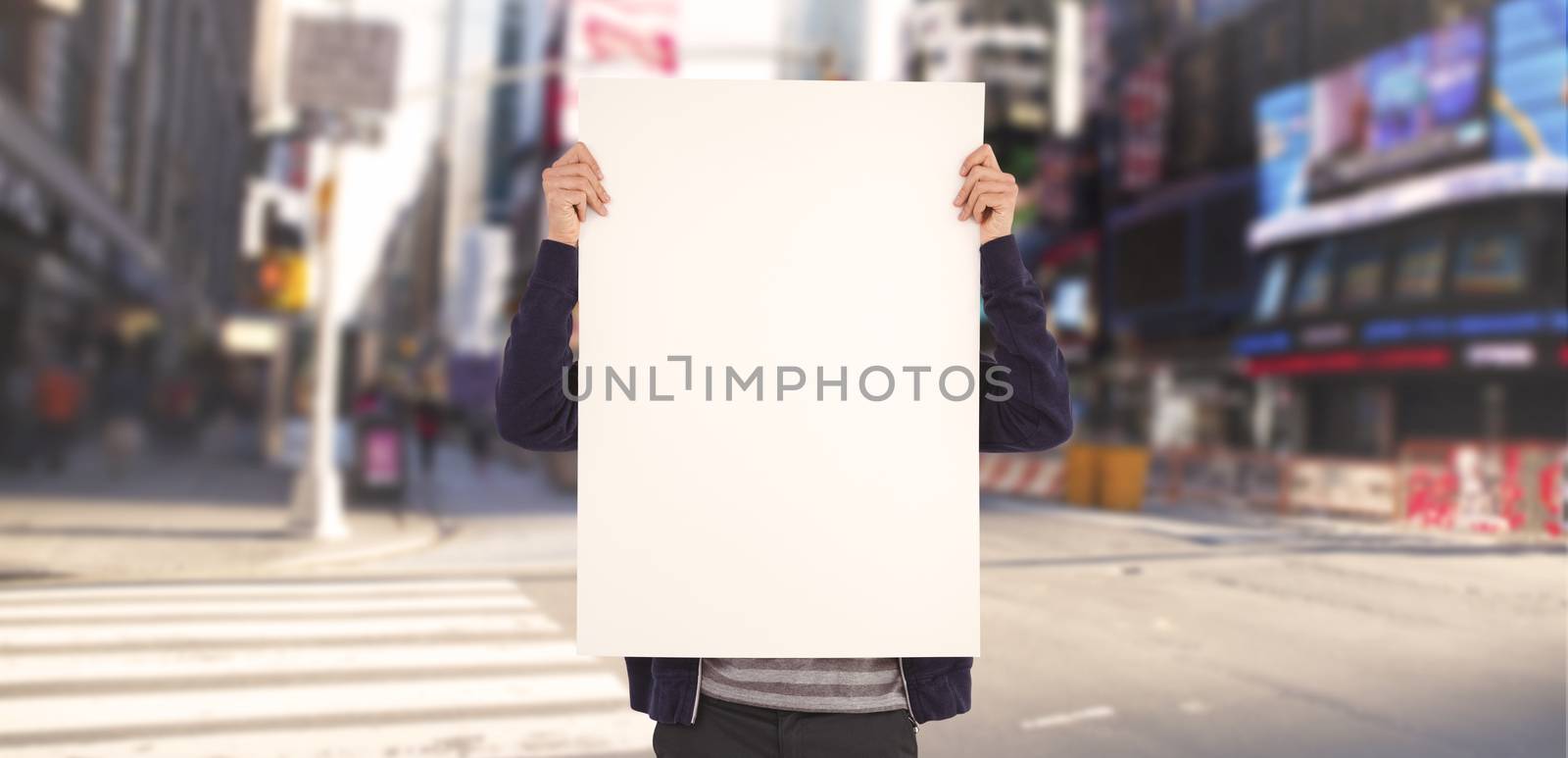 Man showing billboard in front of face against blurry new york street