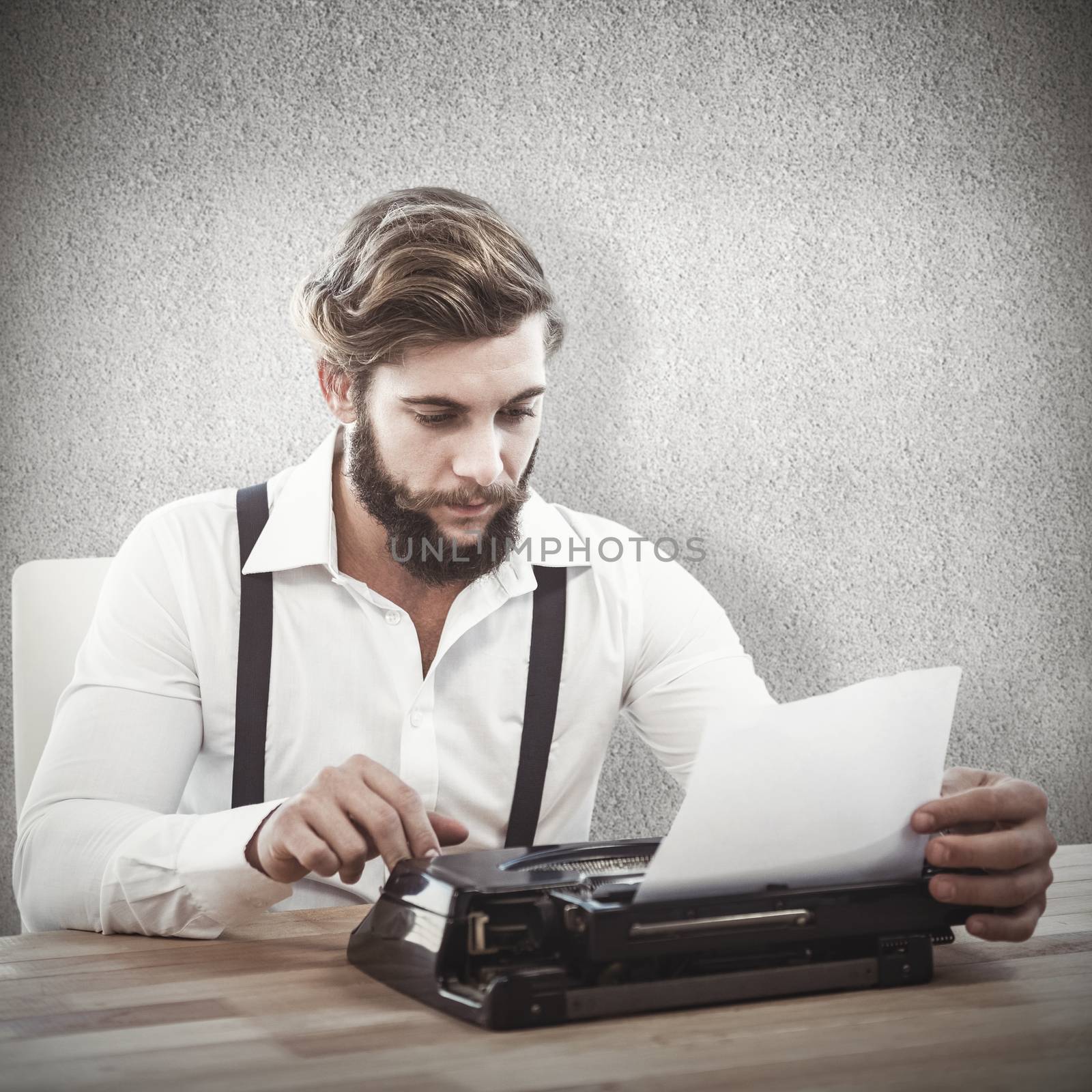 Hipster using typewriter at desk in office against grey wall