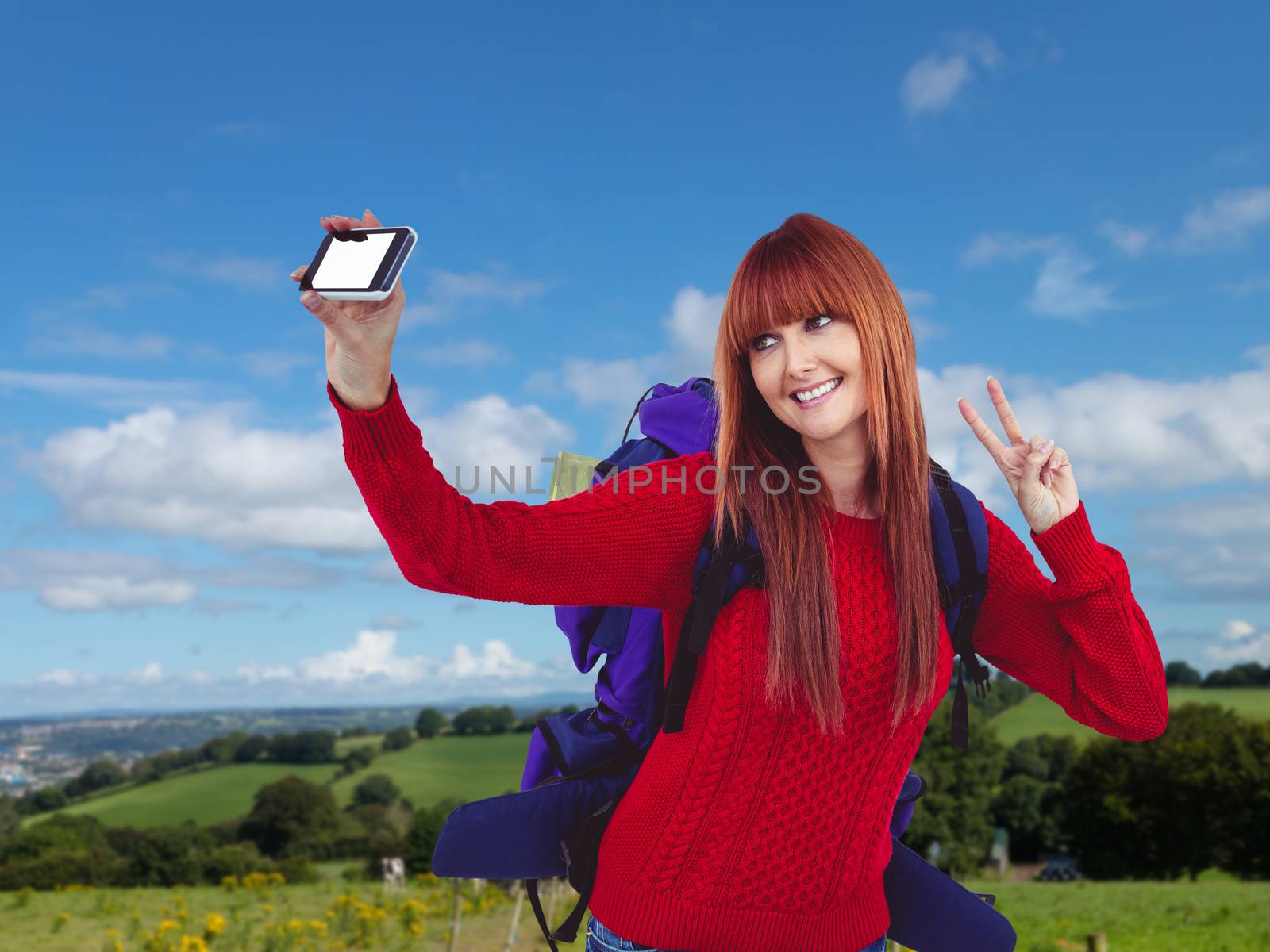 Smiling hipster woman with a travel bag taking selfie against countryside
