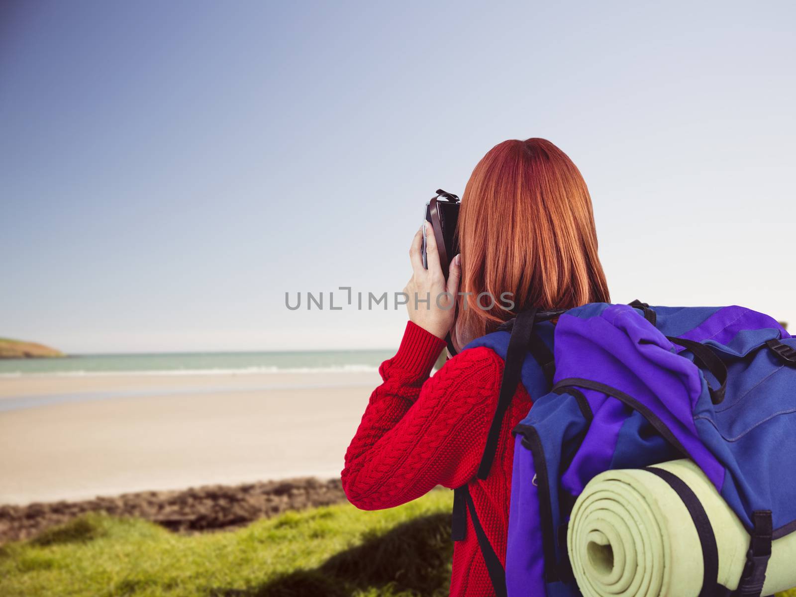 Smiling hipster woman with a travel bag against view of bench close to the beach