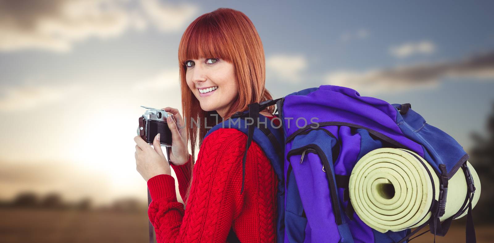 Smiling hipster woman with a travel bag against sunset over a field
