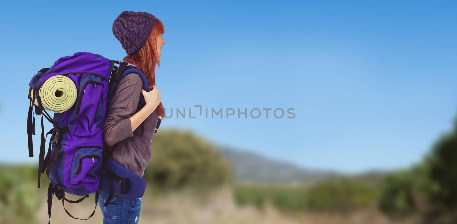 Side view of a hipster woman with a travel bag against mountain trail