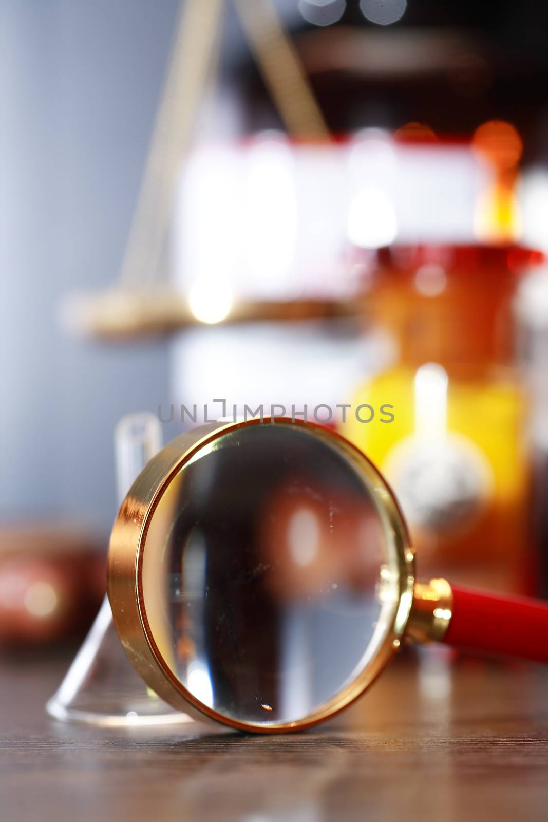 Magnifying glass and chemical funnel against blurred background with old flasks