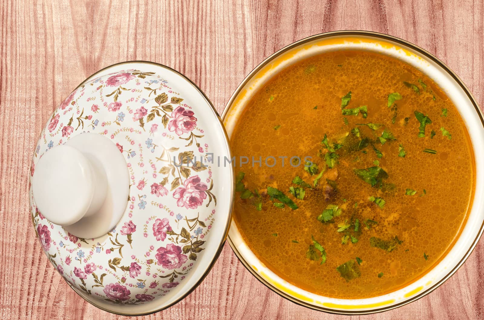 Soup sprinkled with herbs, in a pot with a floral pattern on the colored surface.