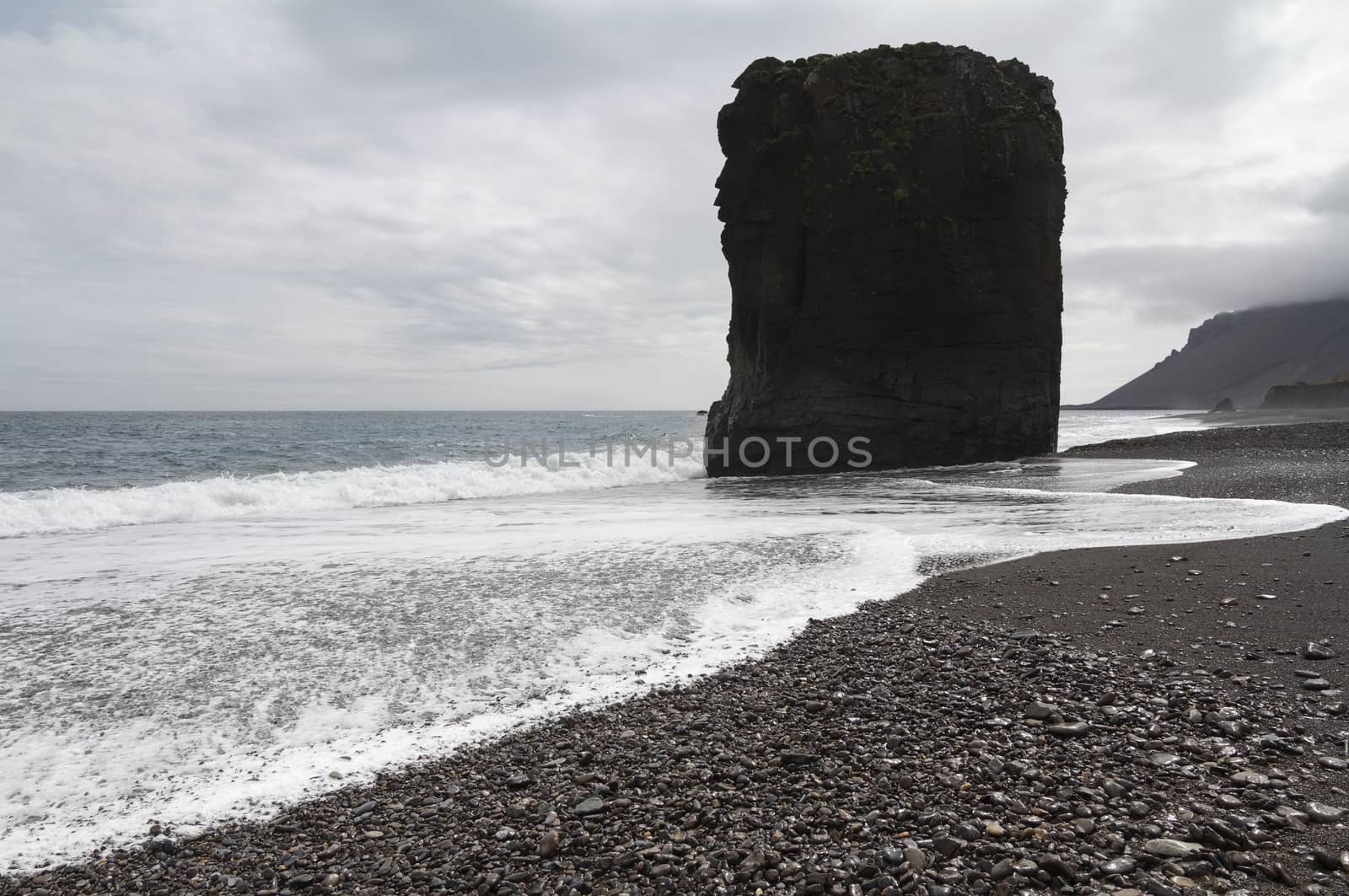 Horizontal view of an Icelandic beach with a huge rock formation in the middle
