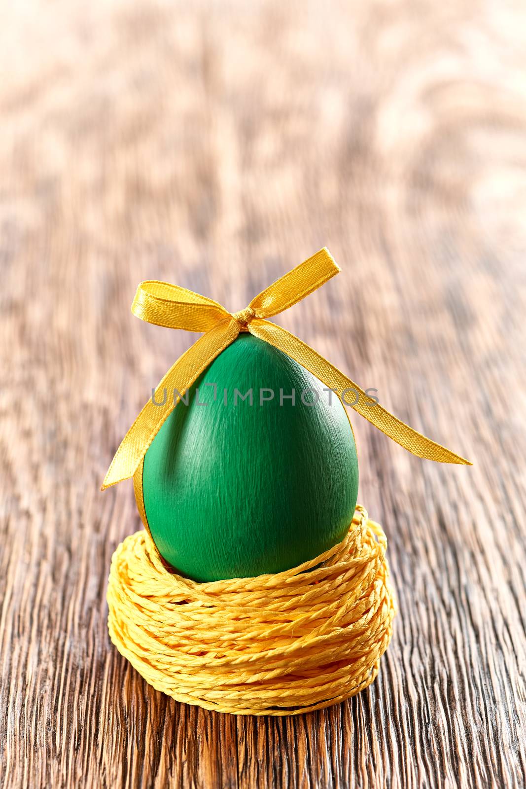 Easter egg in nest. Hand painted decorated egg with bow on wooden background. Unusual creative holiday greeting card 