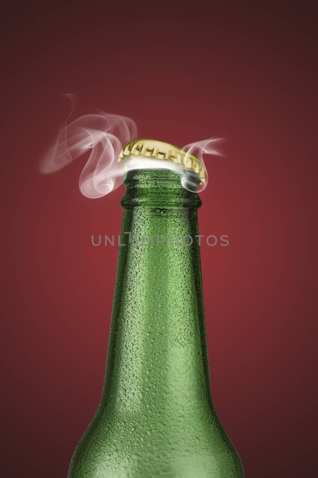 Green cold beer bottle with water drops and golden cap open on red background
