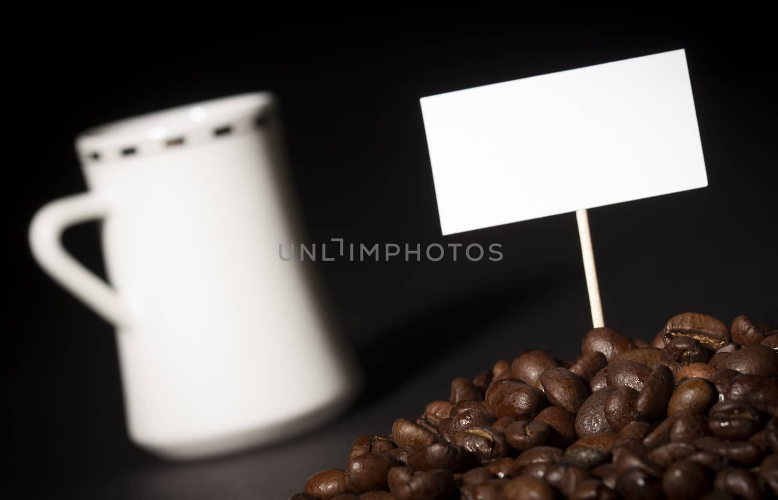 A pile of coffee beans with an empty sign on top of them and a white coffee cup in the background 