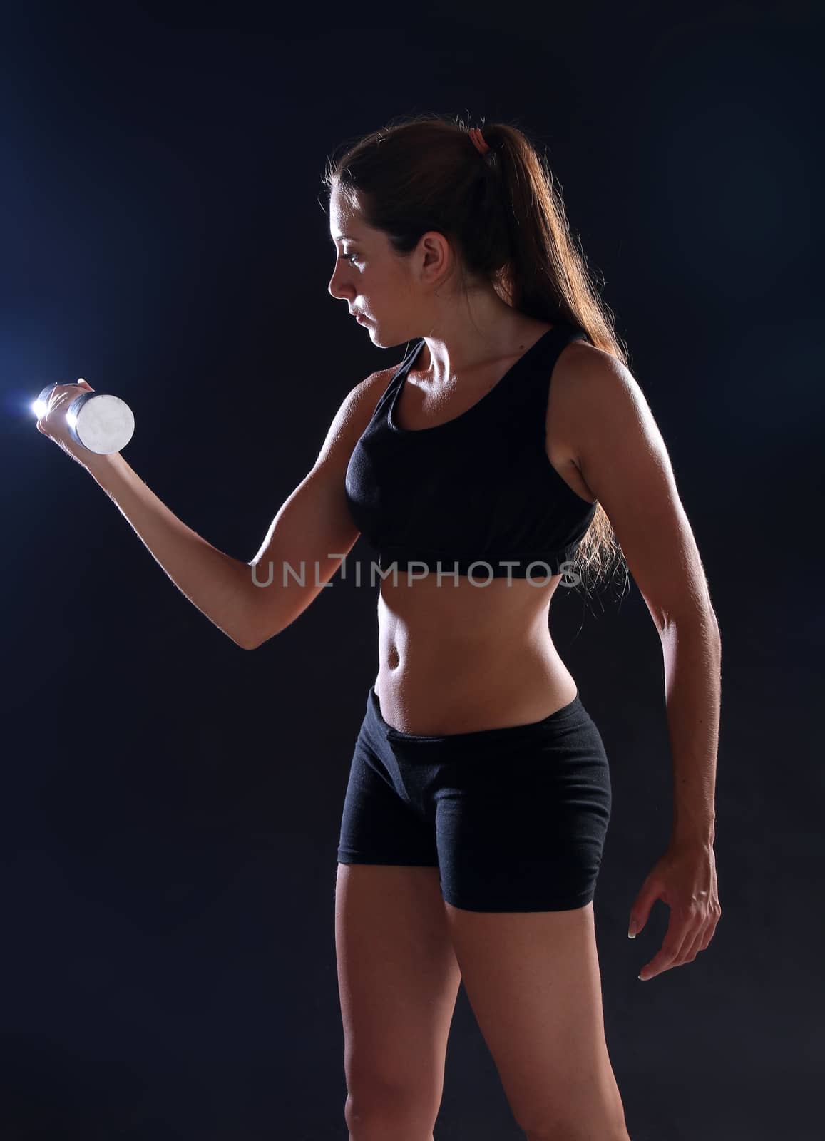 Young woman doing exercise with dumbbells, over black