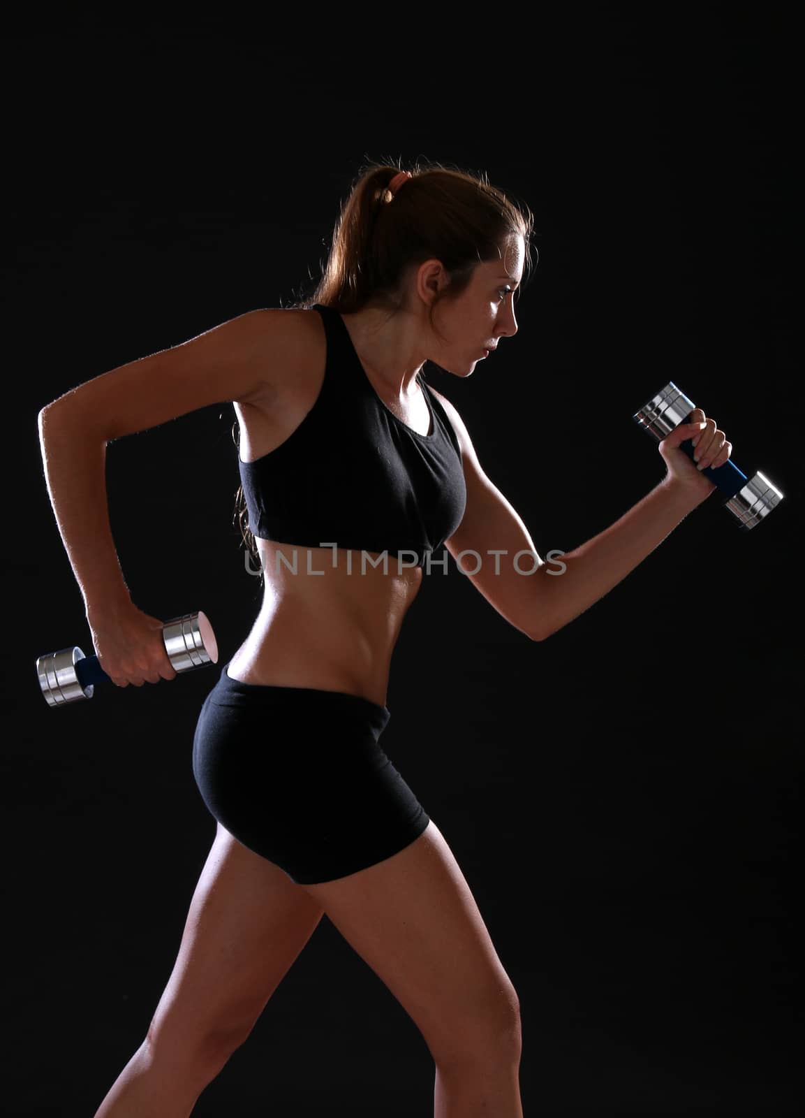 Young woman doing exercise with dumbbells, over black