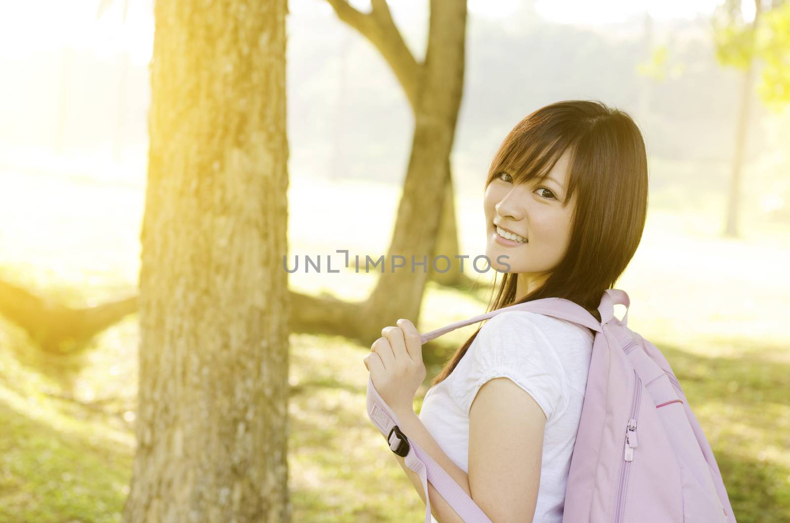 Young Asian university student standing on campus lawn, with backpack and smiling.