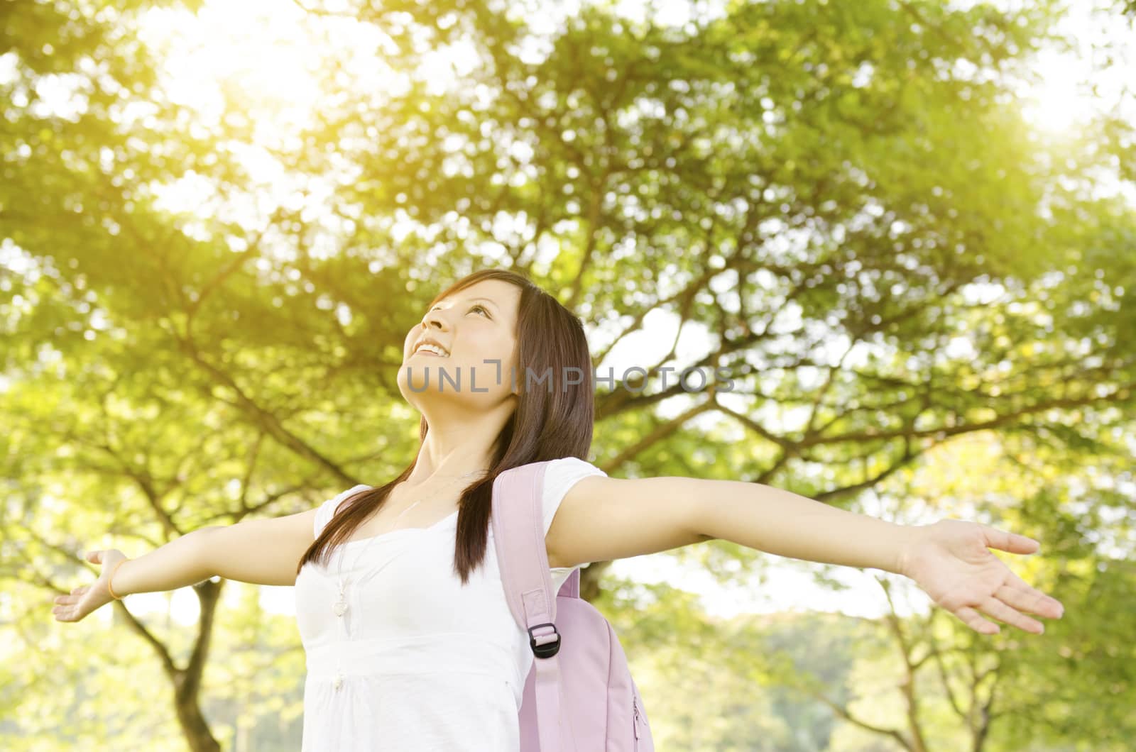 Young Asian college girl student standing on campus lawn, arms outstretched and smiling.