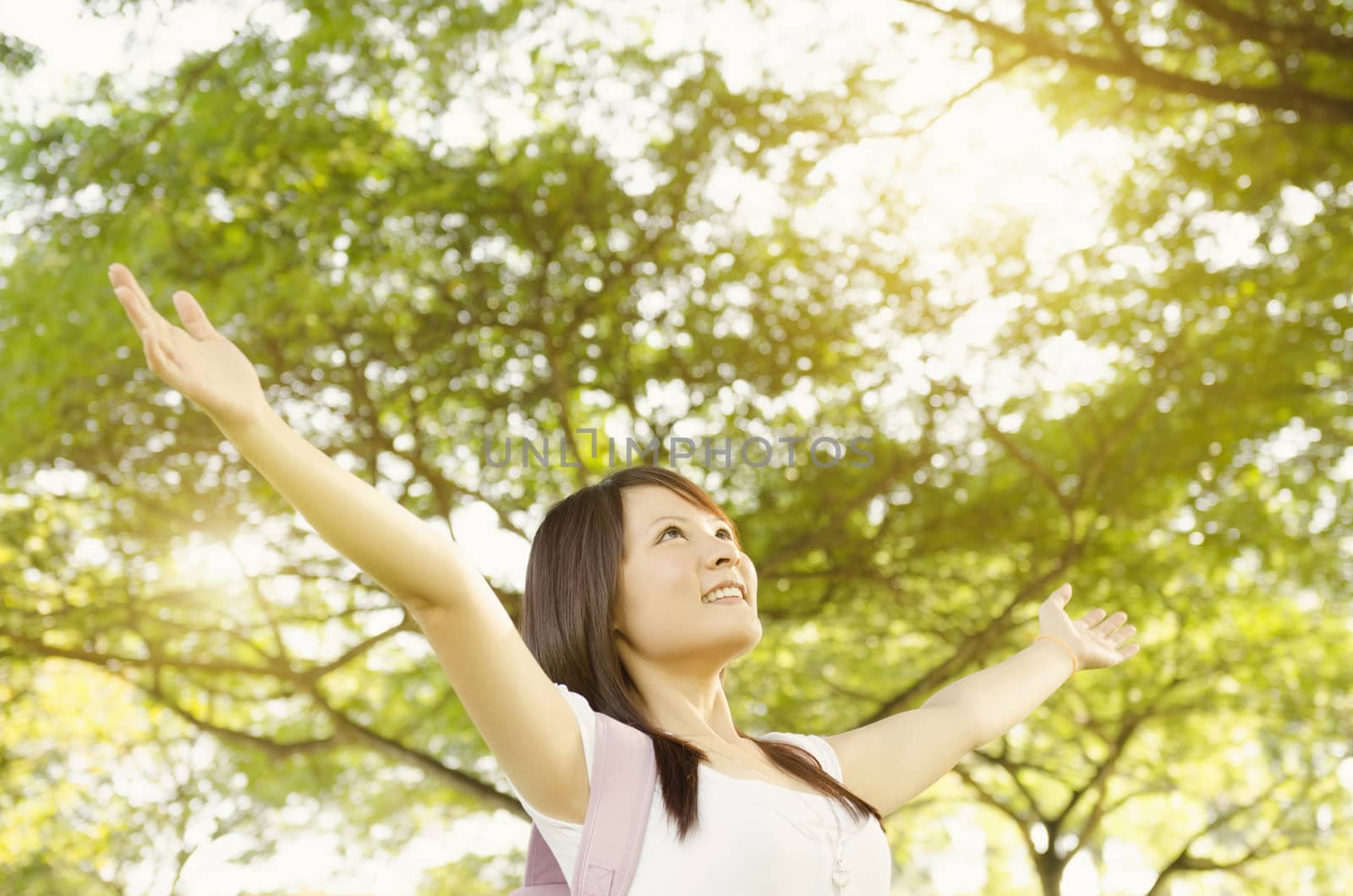 Young Asian university girl student standing on campus lawn, open arms and smiling.