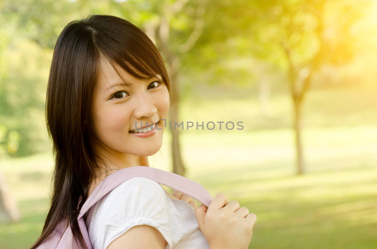 Young Asian adult student standing on campus lawn, with backpack and smiling.