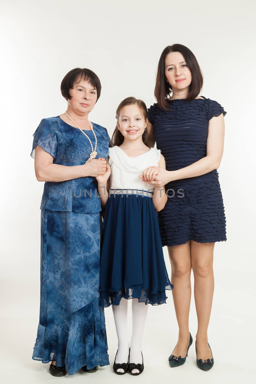 the grandmother, mother and the granddaughter stand in dresses on a white background