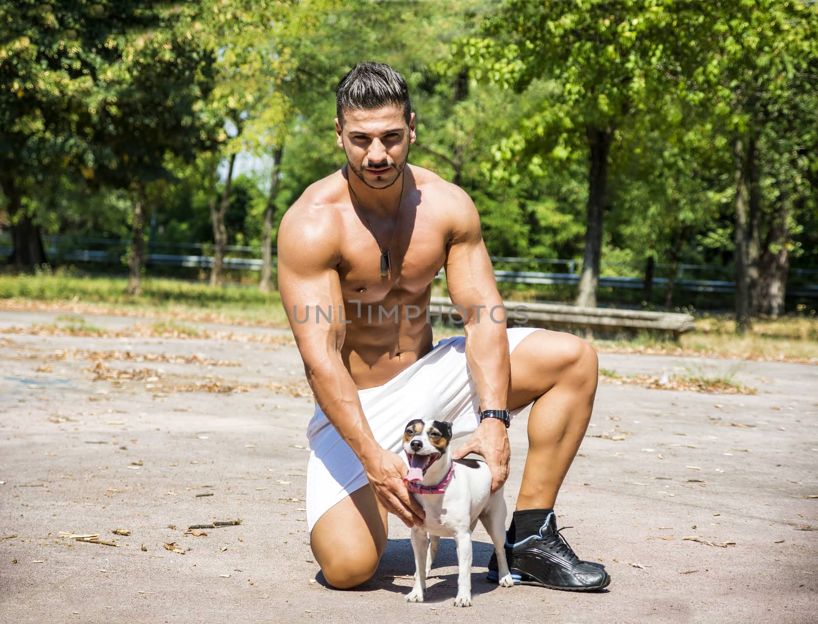 Full Body Shot of a Shirtless Athletic Young Man Kneeling with One Dog, Looking at Camera