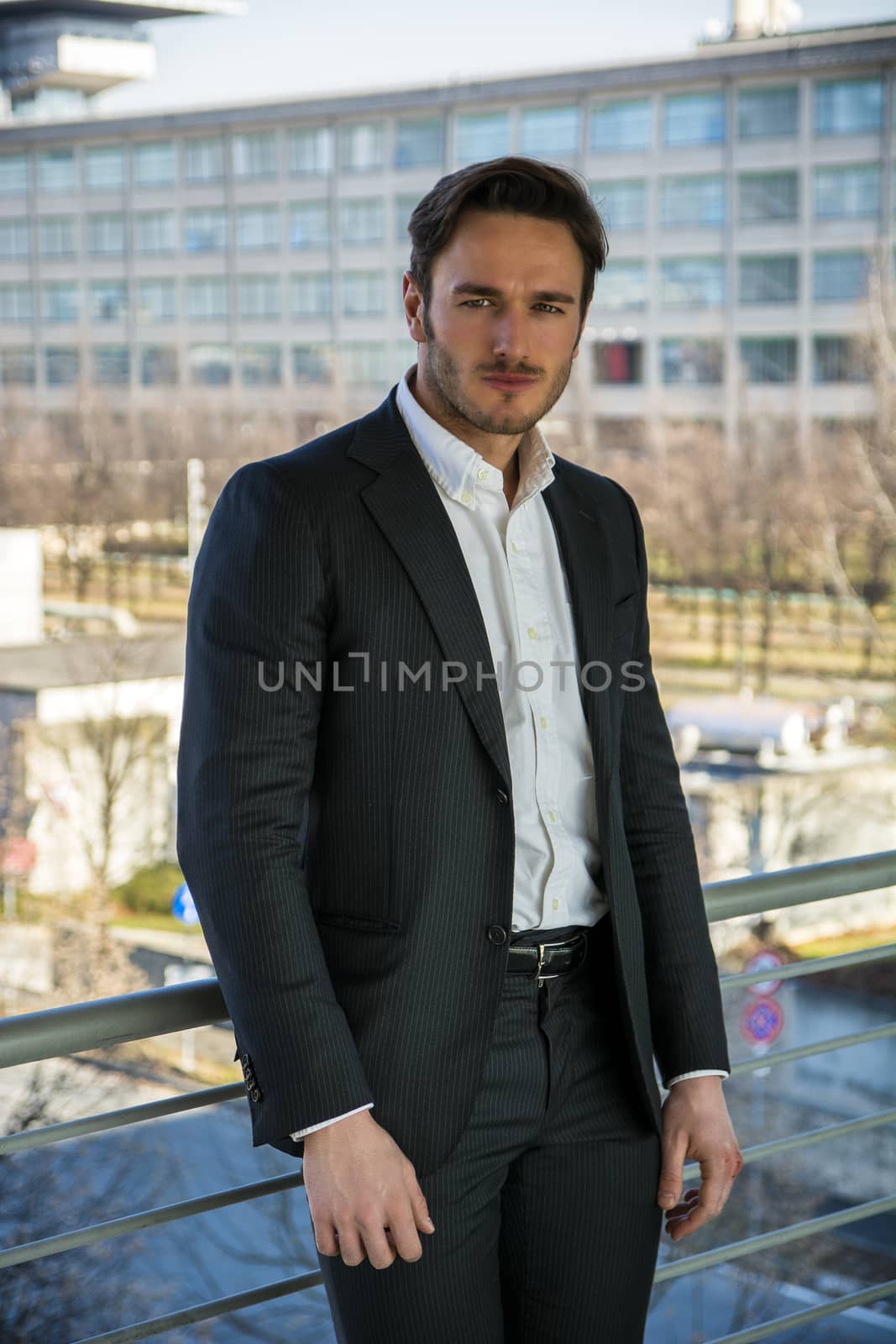 Half body portrait of stylish young man wearing business suit, standing against metal handrail outdoor