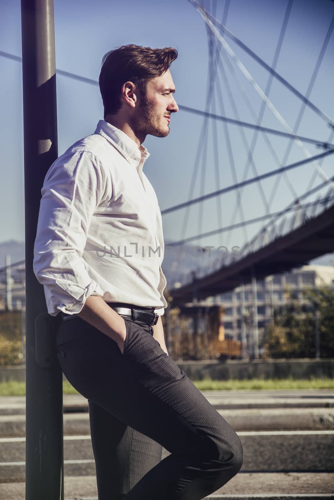 Handsome young man outside wearing white shirt, looking to a side. Profile view, day shot.