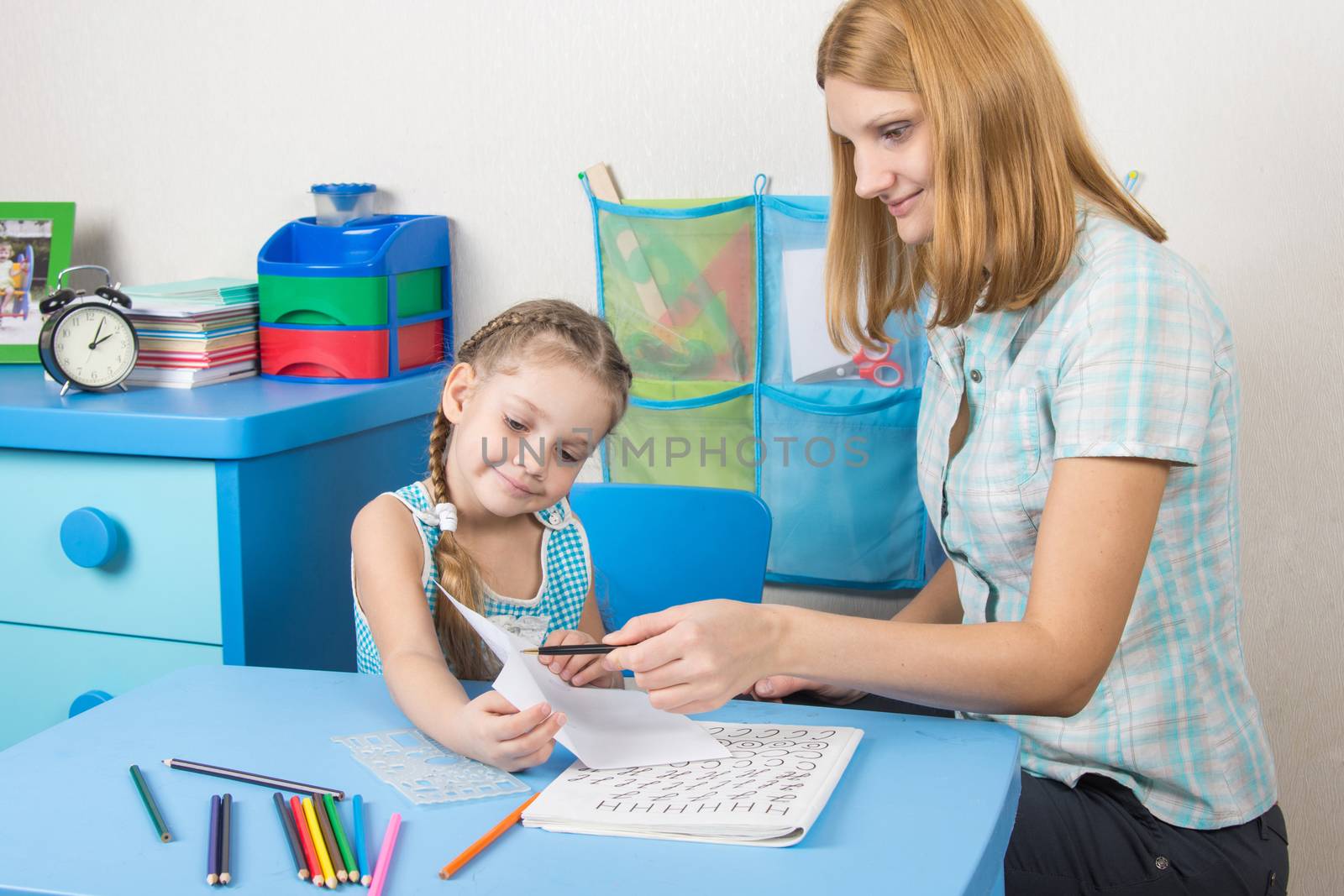 A five-year girl is engaged with adult young beautiful girl sitting at the children table at home