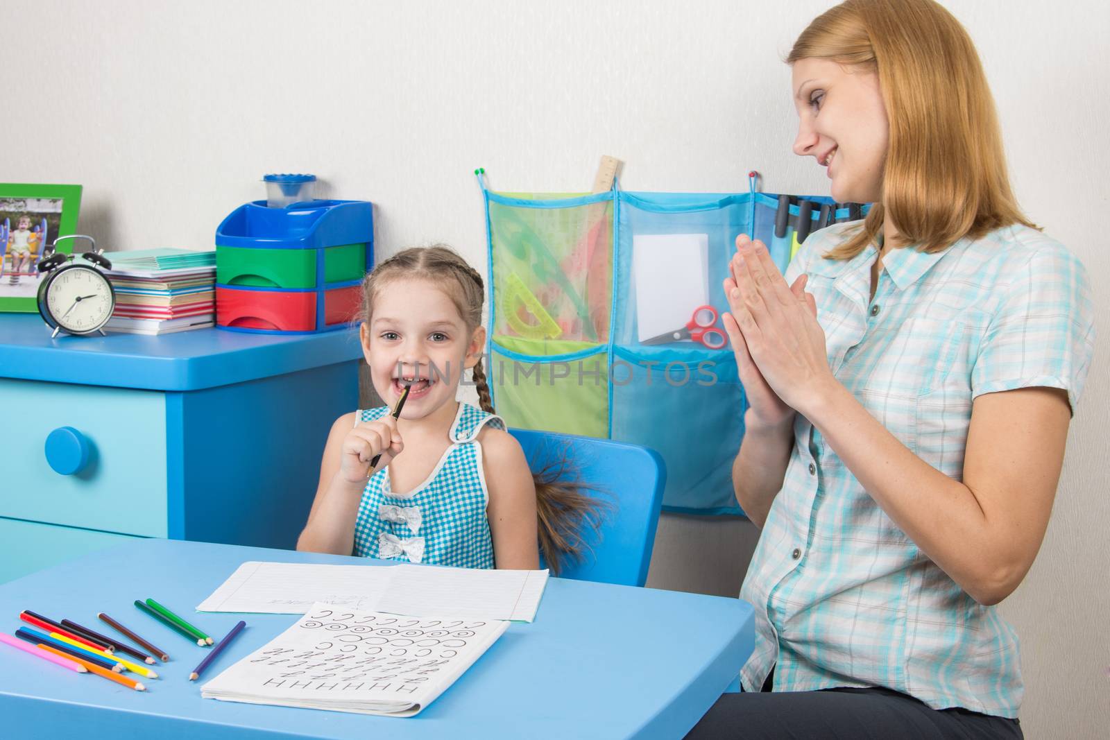 A five-year girl is engaged with adult young beautiful girl sitting at the children table at home