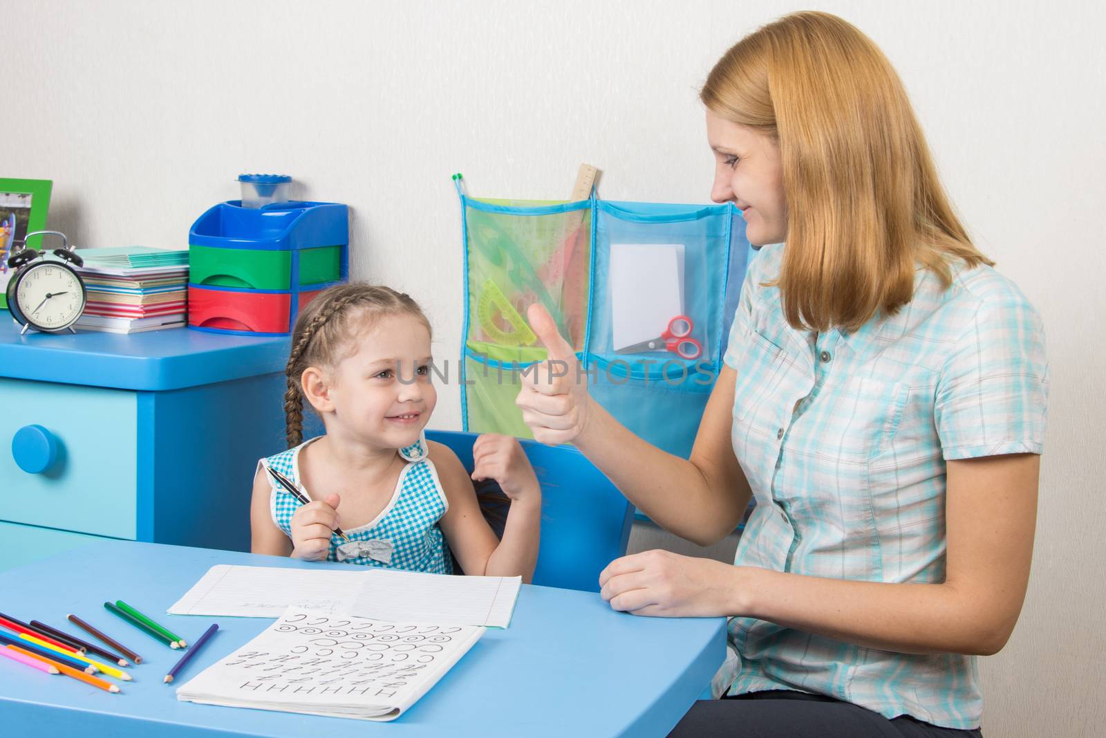 A five-year girl is engaged with adult young beautiful girl sitting at the children table at home