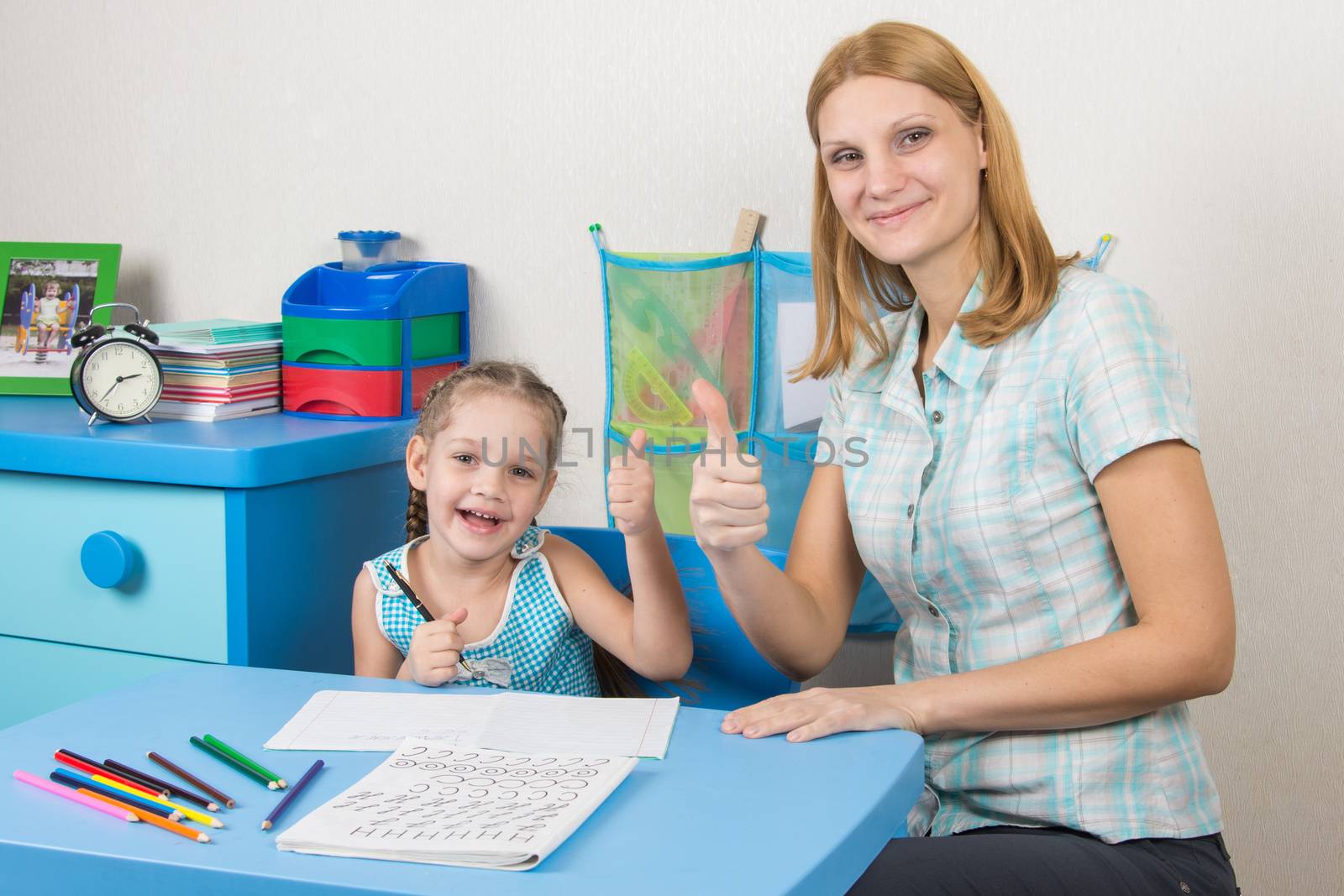 A five-year girl is engaged with adult young beautiful girl sitting at the children table at home