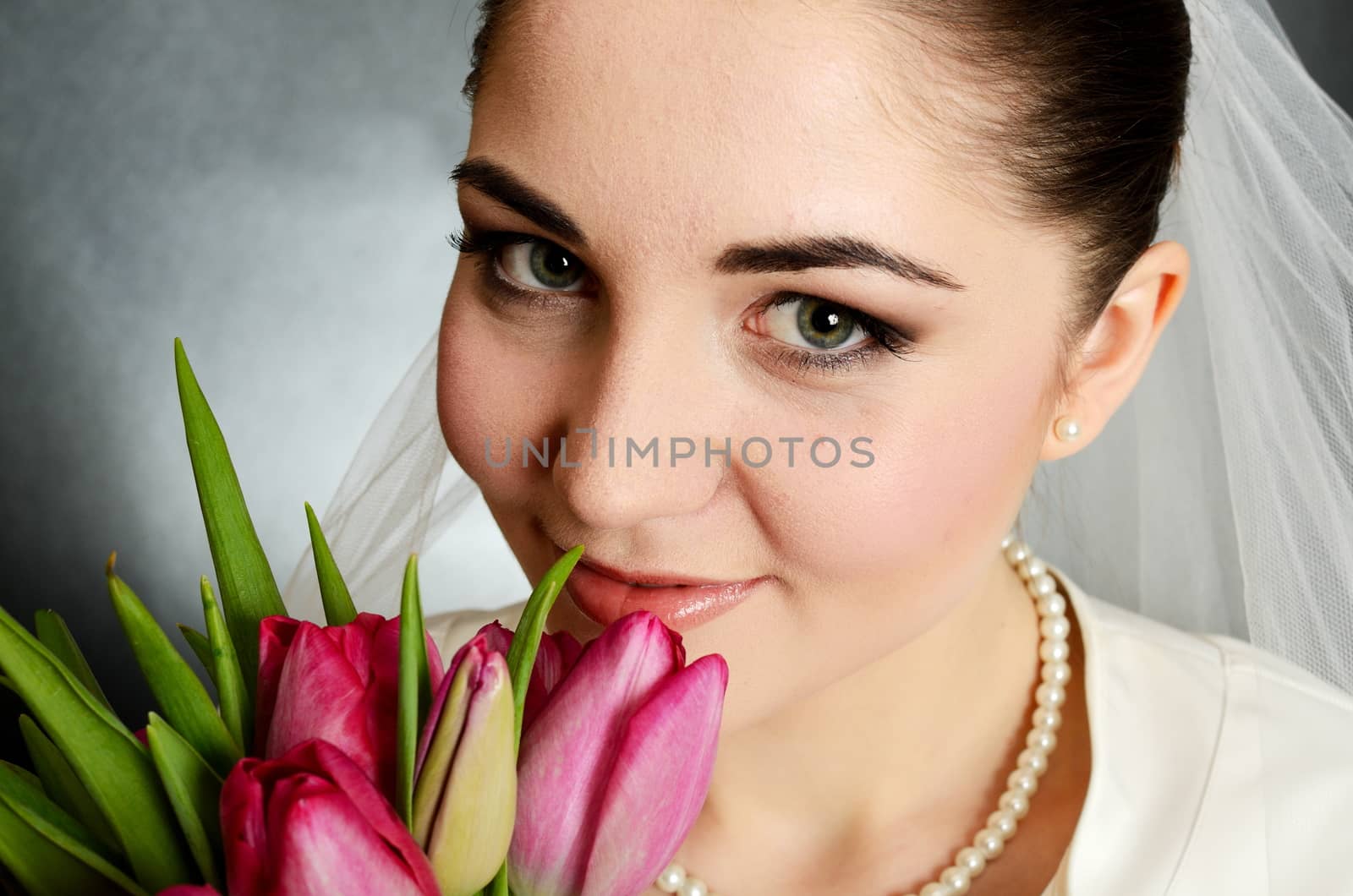 Beautiful, young bride closeup portrait. Young female holding flowers near her face.