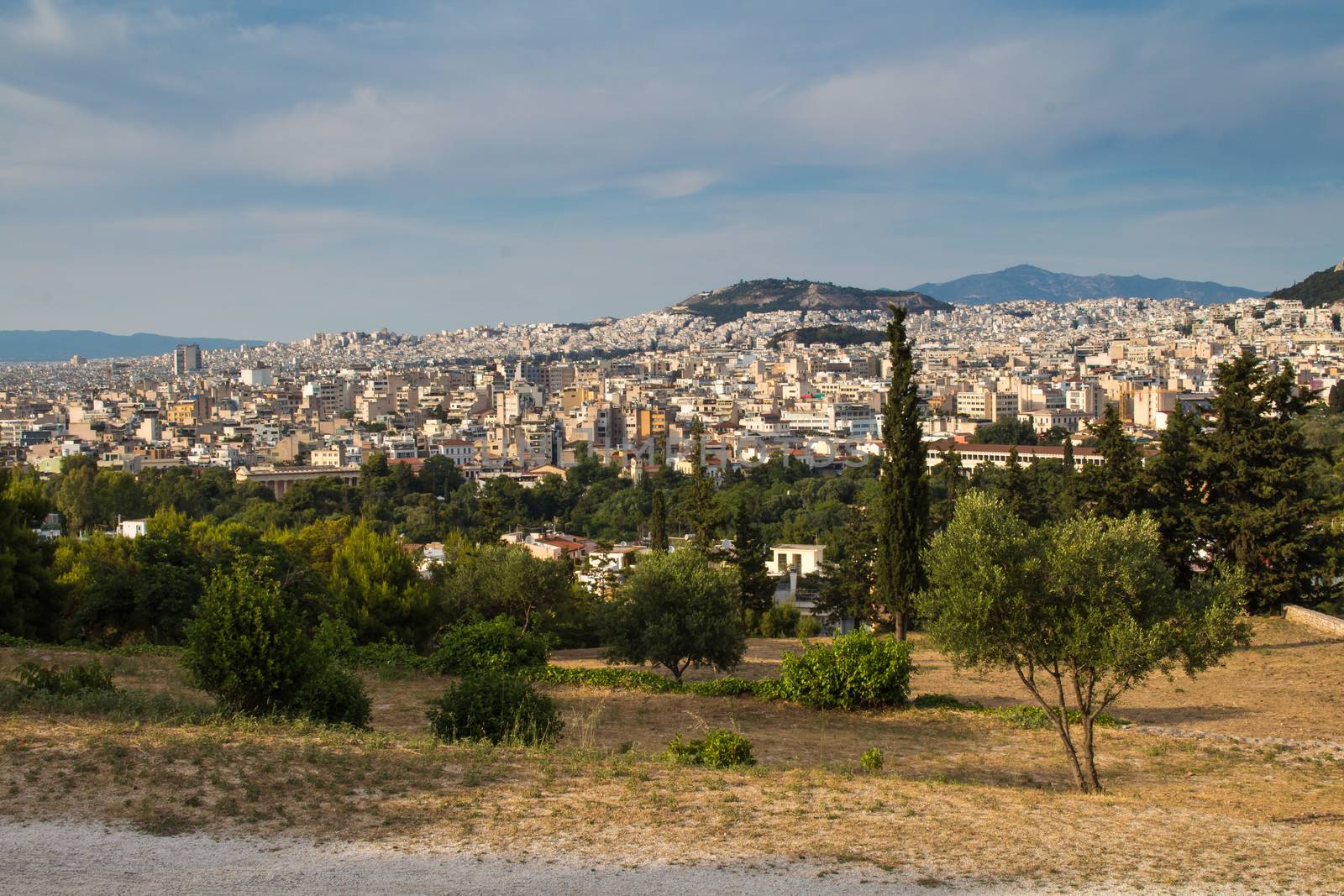 View from a park on a hill on greek capital Athens. Houses climbing up to the hill. Mountains in the background. Cloudy early evening sky.